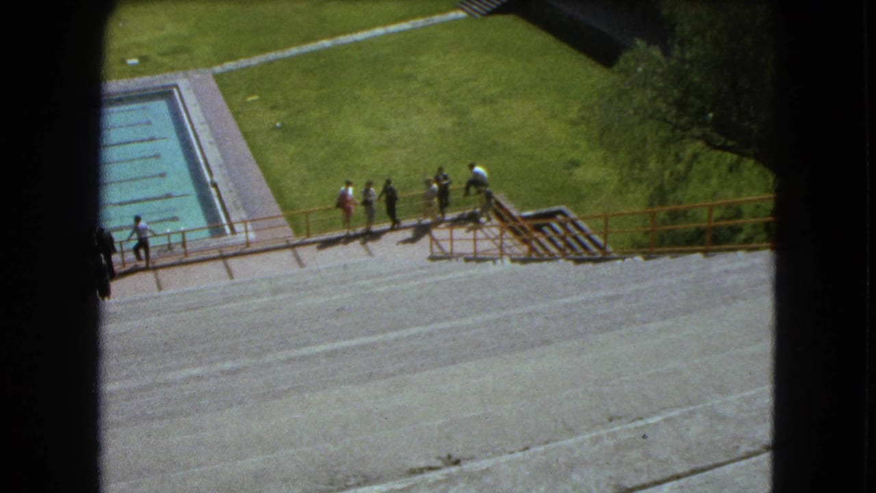 1962 Mexico City 8mm frame showing visitors along a railing overlooking a pool, concrete steps, and lawn.