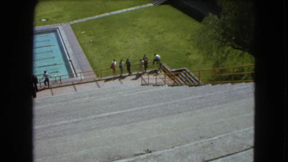 1962 Mexico City 8mm frame showing visitors along a railing overlooking a pool, concrete steps, and lawn.