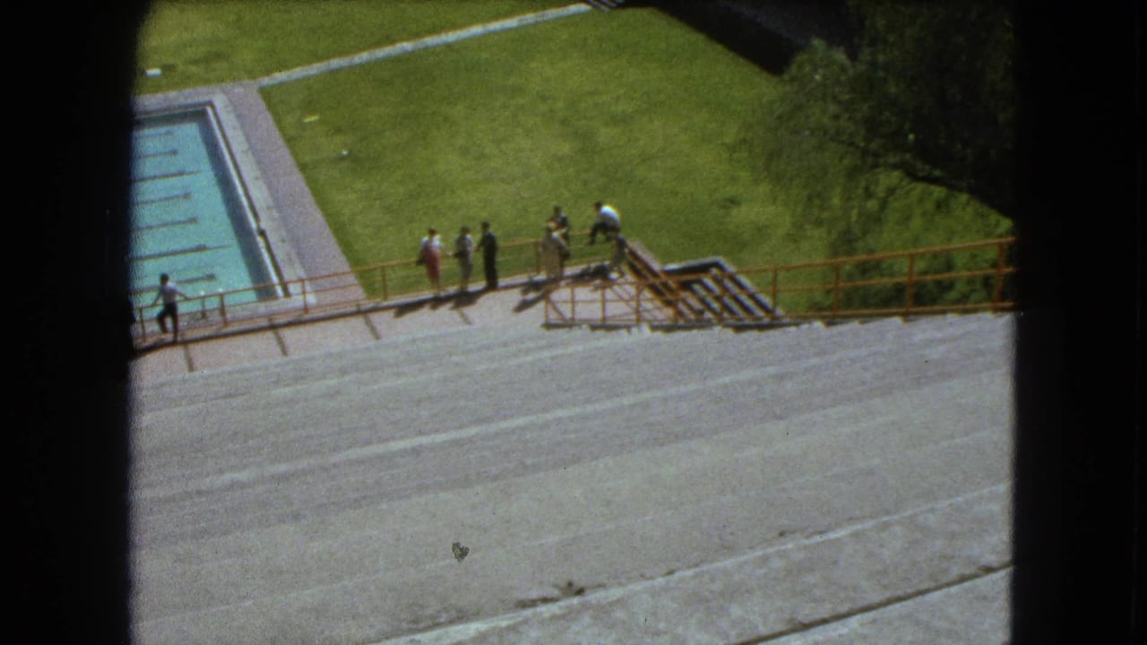 High-angle 1962 Mexico City pool view with people spaced along the railing and lawn beyond.