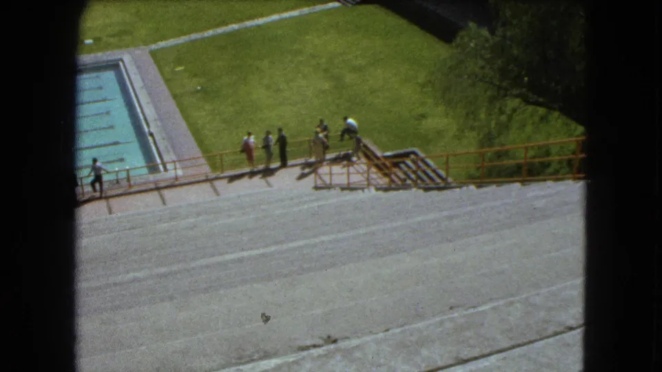 High-angle 1962 Mexico City pool view with people spaced along the railing and lawn beyond.