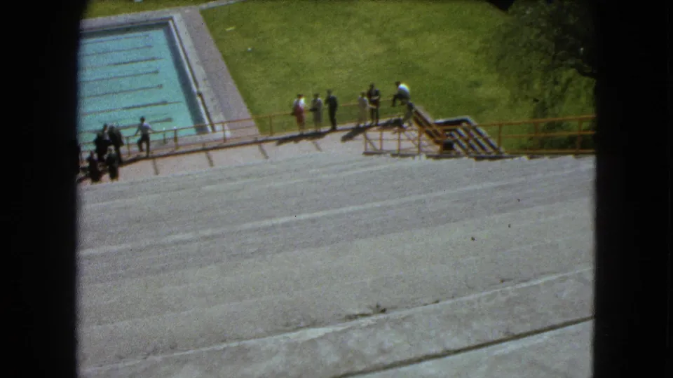 1962 Mexico City home-movie frame with visitors near a railing, a pool corner, stairs, and lawn.