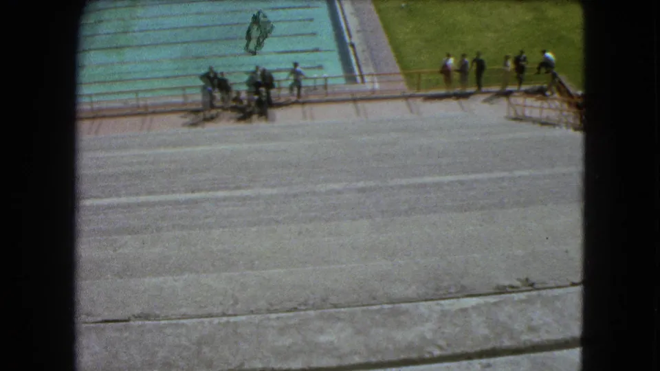 High-angle 1962 Mexico City frame showing a pool, railing, clustered visitors, and broad concrete steps.