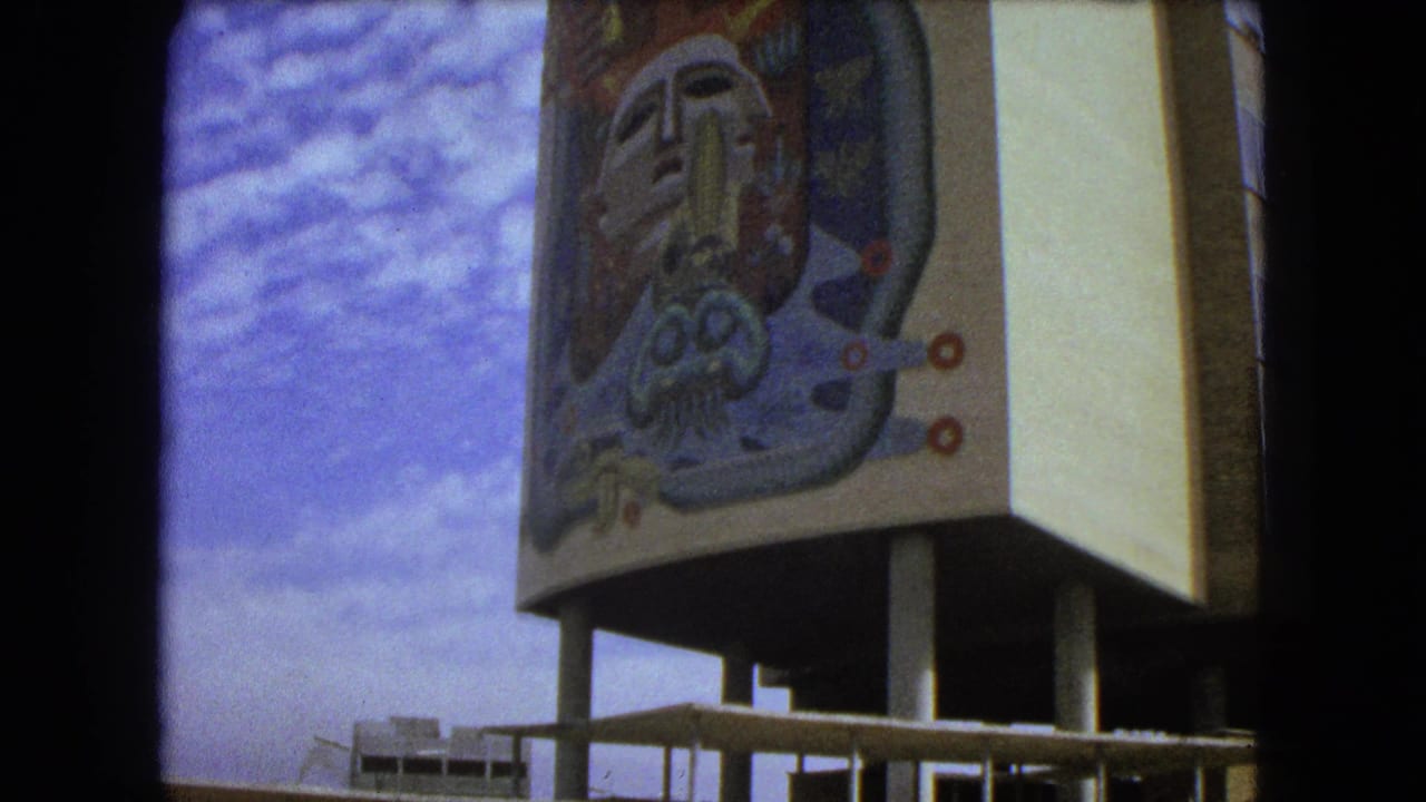 1962 Mexico City home-movie frame showing a muraled modernist building raised on columns beside an open plaza.