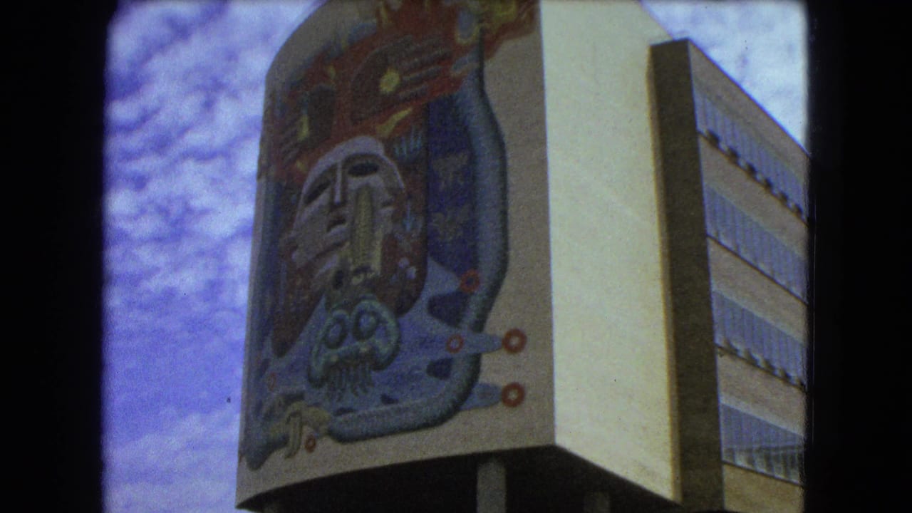 Low-angle view of a building corner with a large colorful stylized face mural under cloudy sky.