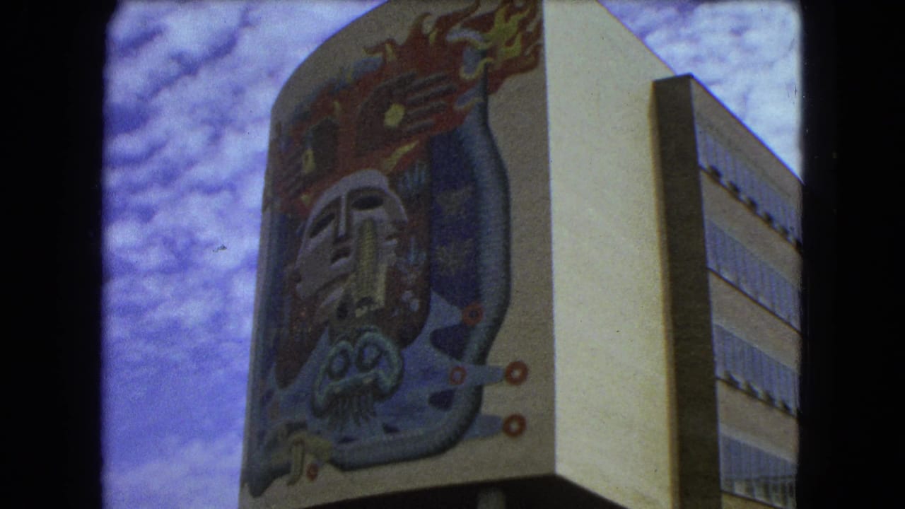 Similar low-angle view of the mural-covered building facade with windows at right and cloudy sky behind.