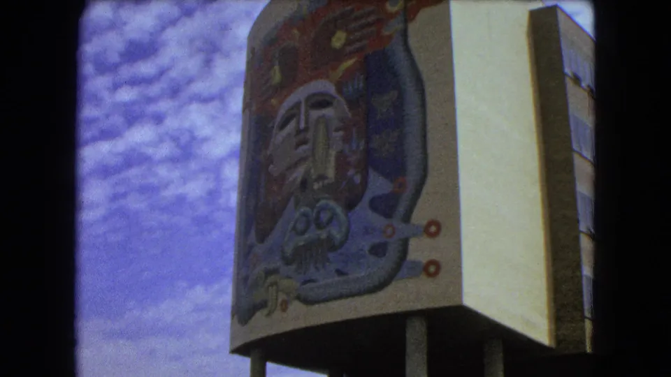 Final 1962 Mexico City frame showing the mural-covered building facade from below, with soft grain, cloudy sky, and visible film gate edges.