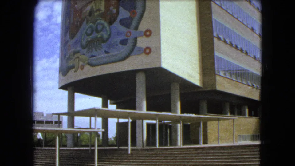 1962 Mexico City footage showing a closer building corner with an abstract mural, exterior stairs, columns, and walkway.
