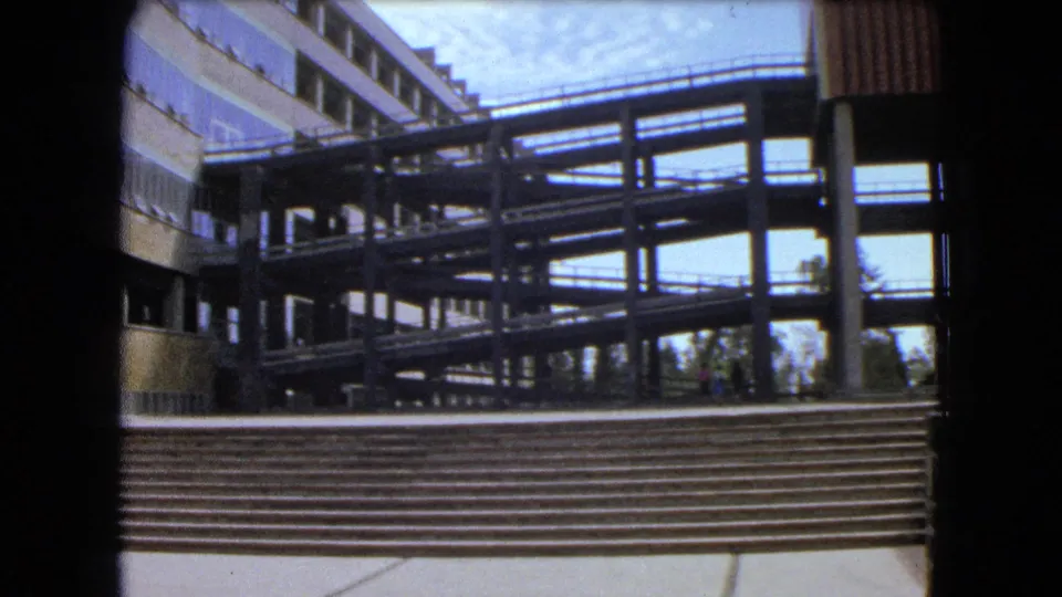 The frame shows mid-century modern walkways and ramps above broad steps in Mexico City, with small pedestrians near the base.