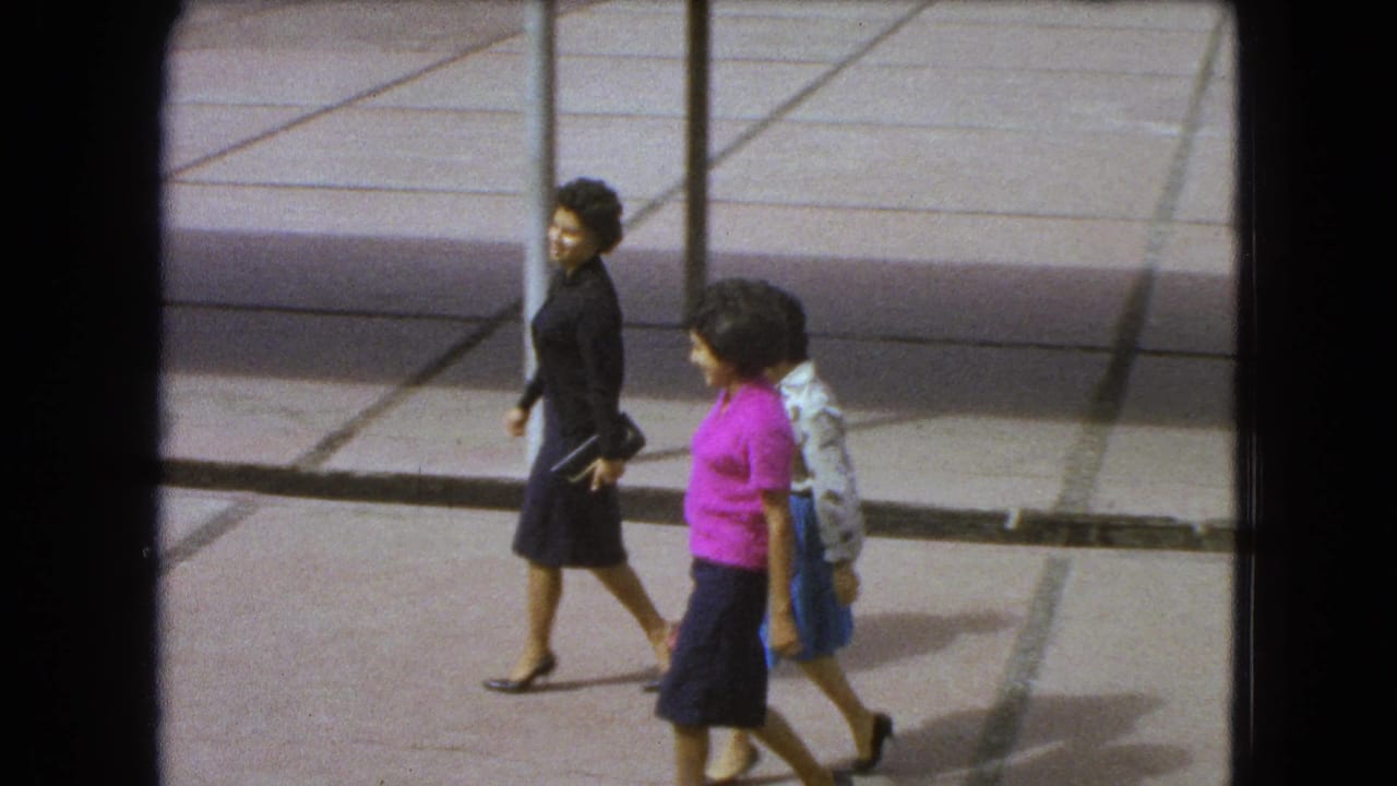 Three women in professional-looking 1960s attire walk through a modern Mexico City courtyard with geometric paving.