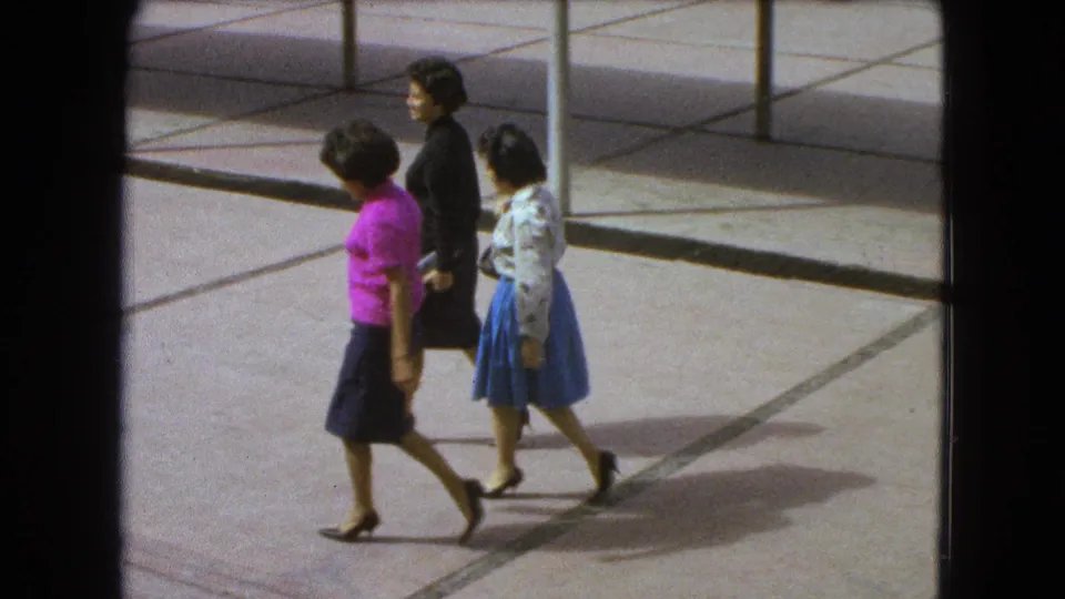 Three professional-looking women walk through a sunlit Mexico City courtyard, framed by 8mm film borders and long shadows.