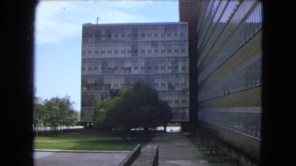 1962 Mexico City 8mm view of a large concrete building, lawn, trees, and a walkway seen from a shaded opening.