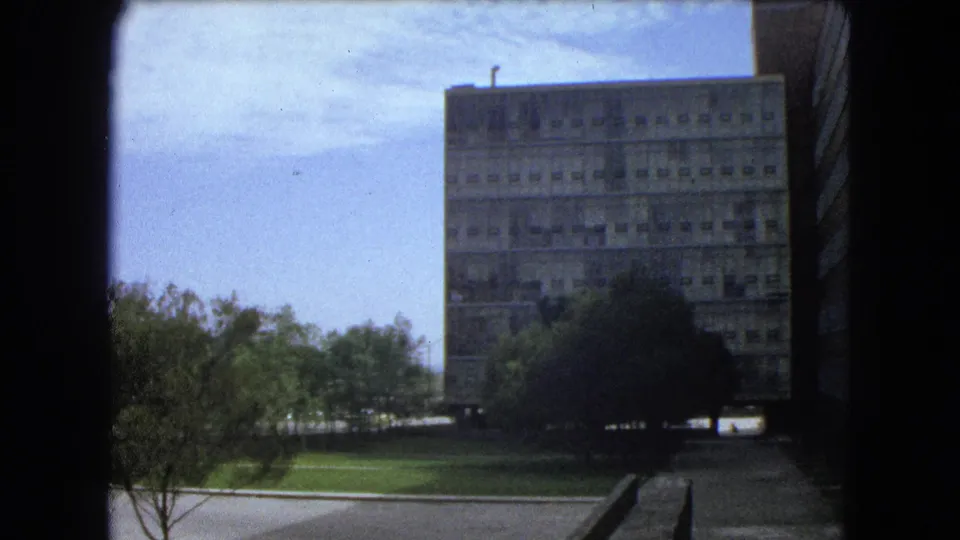 Handheld 8mm frame from Mexico City showing a concrete building, surrounding greenery, and paved circulation paths in 1962.