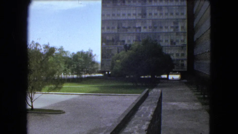 Final 1962 Mexico City frame shows the large concrete building with trees, lawn, walkway, and side wall under bright sky.