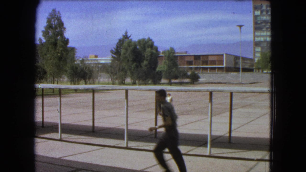 A person runs across the foreground of a 1962 Mexico City school campus, with railings, trees, and buildings behind.