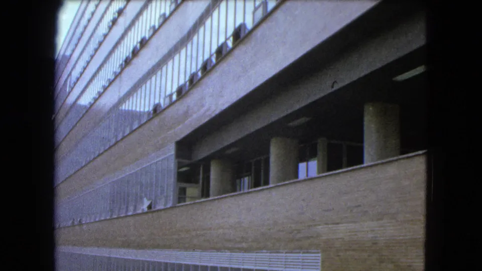 Angled 1962 Mexico City campus facade with concrete columns, brick wall, upper railing, and repeated window lines.