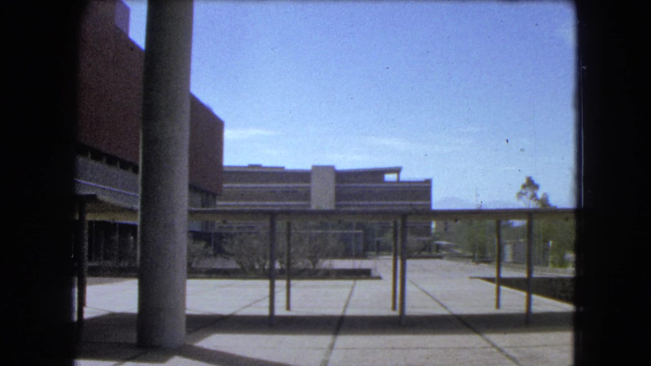 1962 Mexico City exterior with a modern brick building, concrete column, covered walkway, paved plaza, and sparse trees.