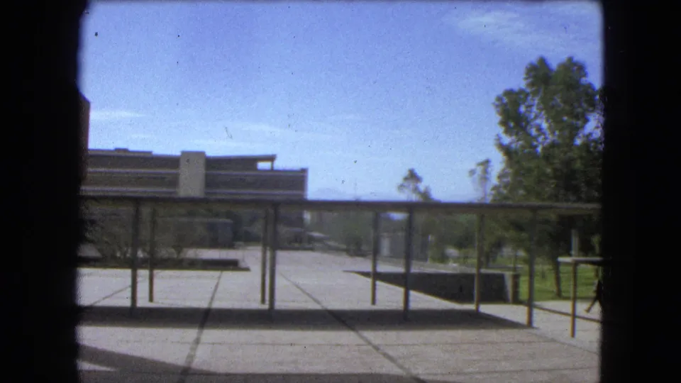 1962 Mexico City courtyard view showing the walkway structure, paved ground, brick building edge, trees, lawn, and distant hills or skyline.