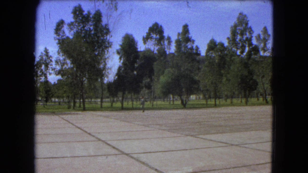 Open concrete walkway with trees and a small figure moving across the background.
