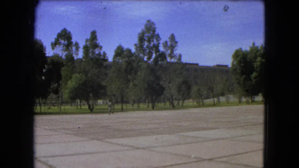Mexico City 1962 frame with a wide paved foreground, tree border, and a distant man walking through the public space.