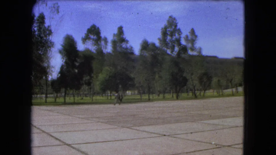 End frame of a 1962 Mexico City plaza shot, with one distant man walking near the trees and broad paving filling the foreground.