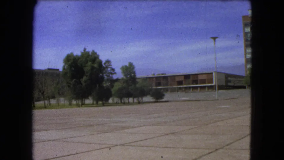 1962 Mexico City 8mm frame showing a broad paved area, planted trees, a low building, lamppost, and partial high-rise.