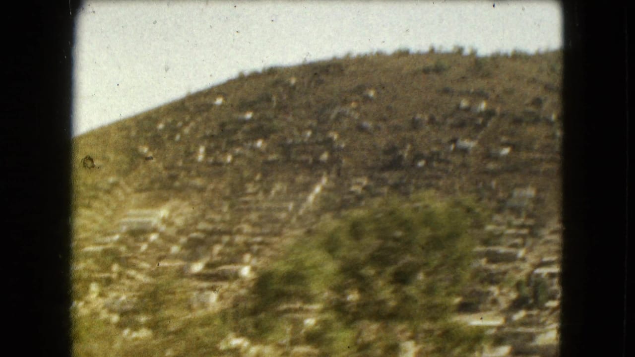 1962 Mexico City home-movie frame showing a passing hillside and roadside through the bars of a moving vehicle window.