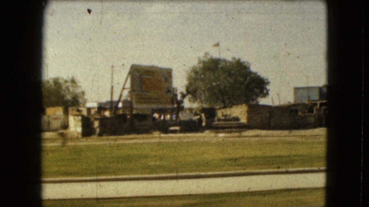 White billboard structure, low brown building, trees, and roadside grass.
