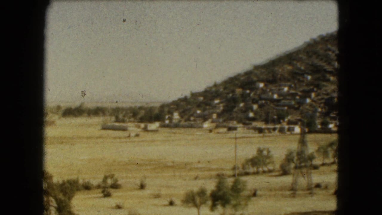 Hillside homes at right with open dry terrain, trees, and utility structures in the foreground.