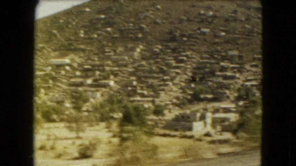 1962 Mexico City 8mm frame showing dense small homes on a hillside, with dry terrain and trees in the foreground.