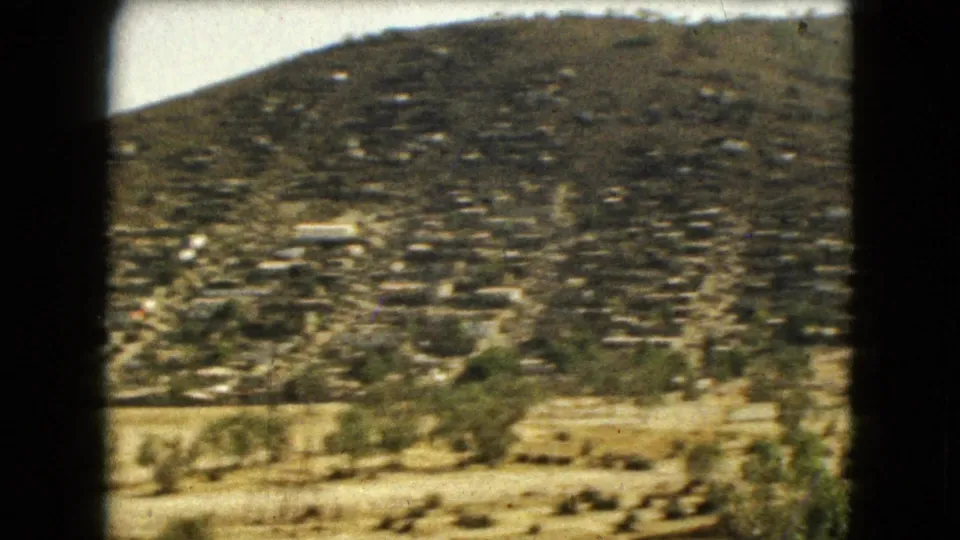 A shaky 1962 Mexico City home-movie view across barren foreground land toward dense hillside housing.