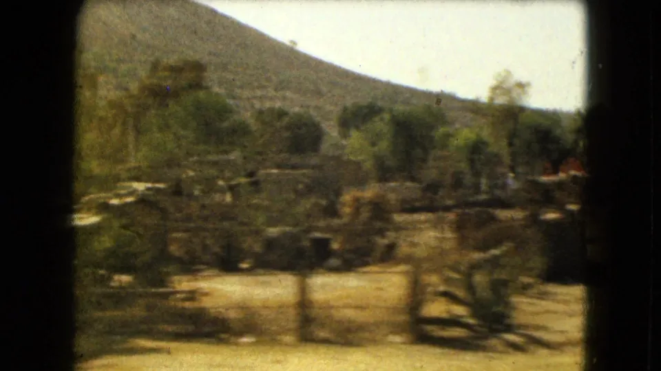 Motion-blurred 8mm frame of hillside, trees, scrub, and low walls along a rural route near Mexico City in 1962.