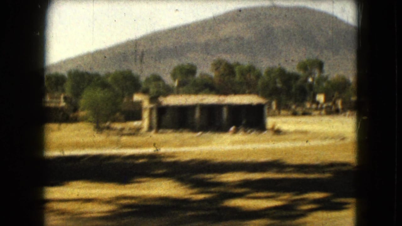 Low rural structure and trees in front of a mountain slope.