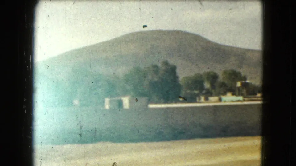 Faded 1962 Mexico City home-movie frame showing trees and low structures through haze with a mountain slope behind.