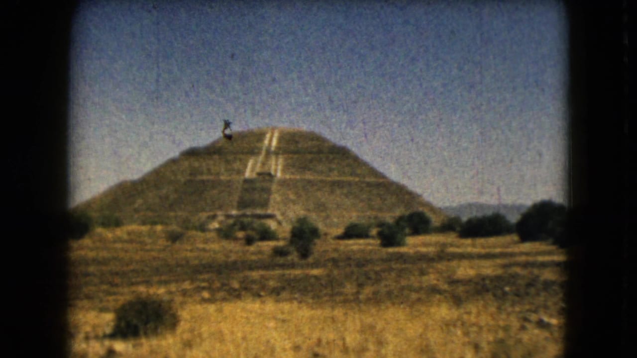 Stepped pyramid across dry grassland beneath a blue sky, framed by dark film edges.
