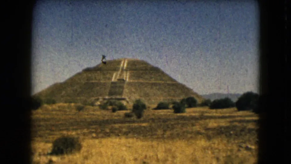 1962 8mm view of the Pyramid of the Sun area at Teotihuacan, seen from dry grassland with shrubs and distant hills.