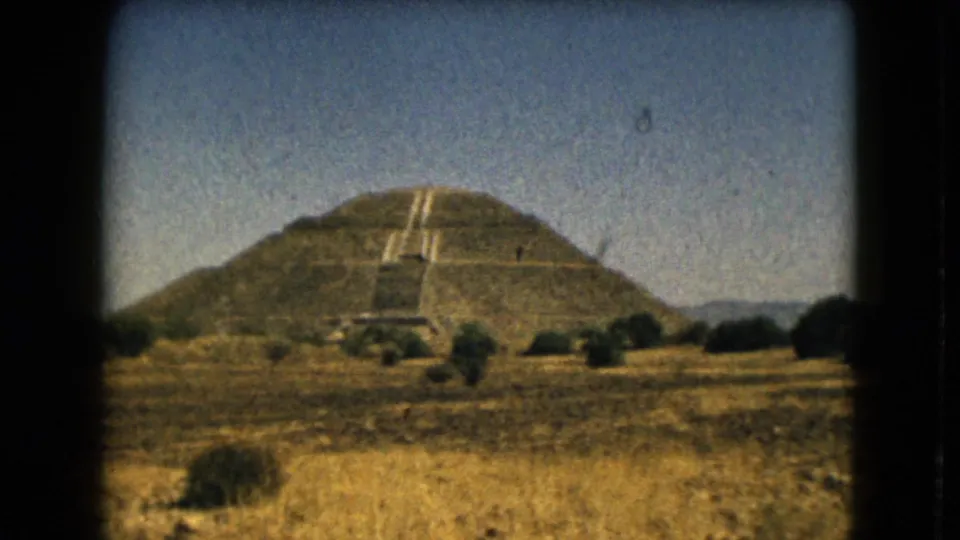 Grainy 1962 8mm view of the Pyramid of the Sun area, with dry vegetation in front and low hills behind.
