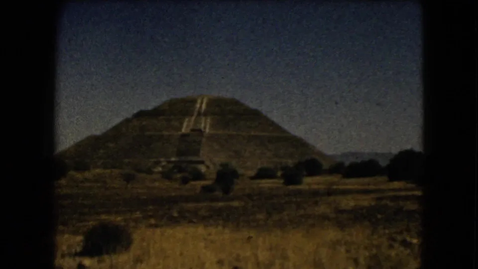 A stepped Mesoamerican pyramid near Mexico City appears beyond dry grass in warm 8mm color.