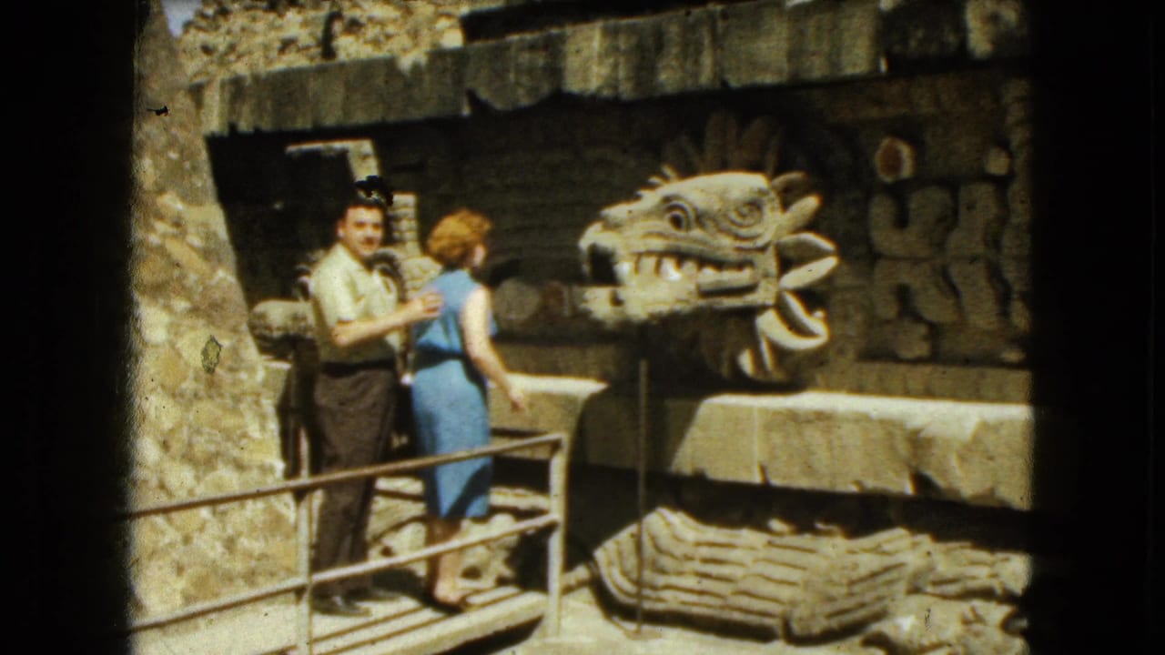 Man and woman stand on a walkway beside a large carved serpent-head sculpture.