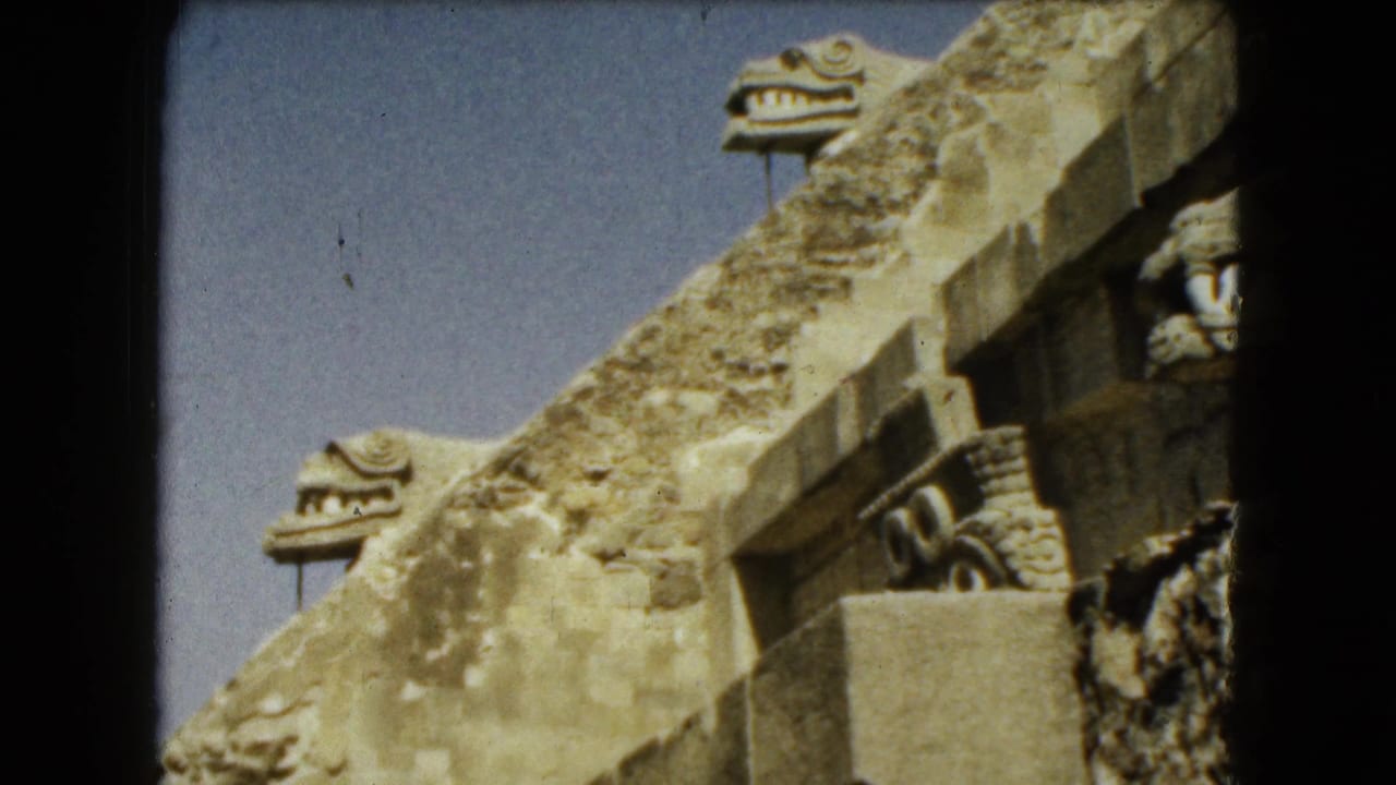Stone ruin wall with carved serpent-like heads and a shadowed film edge.
