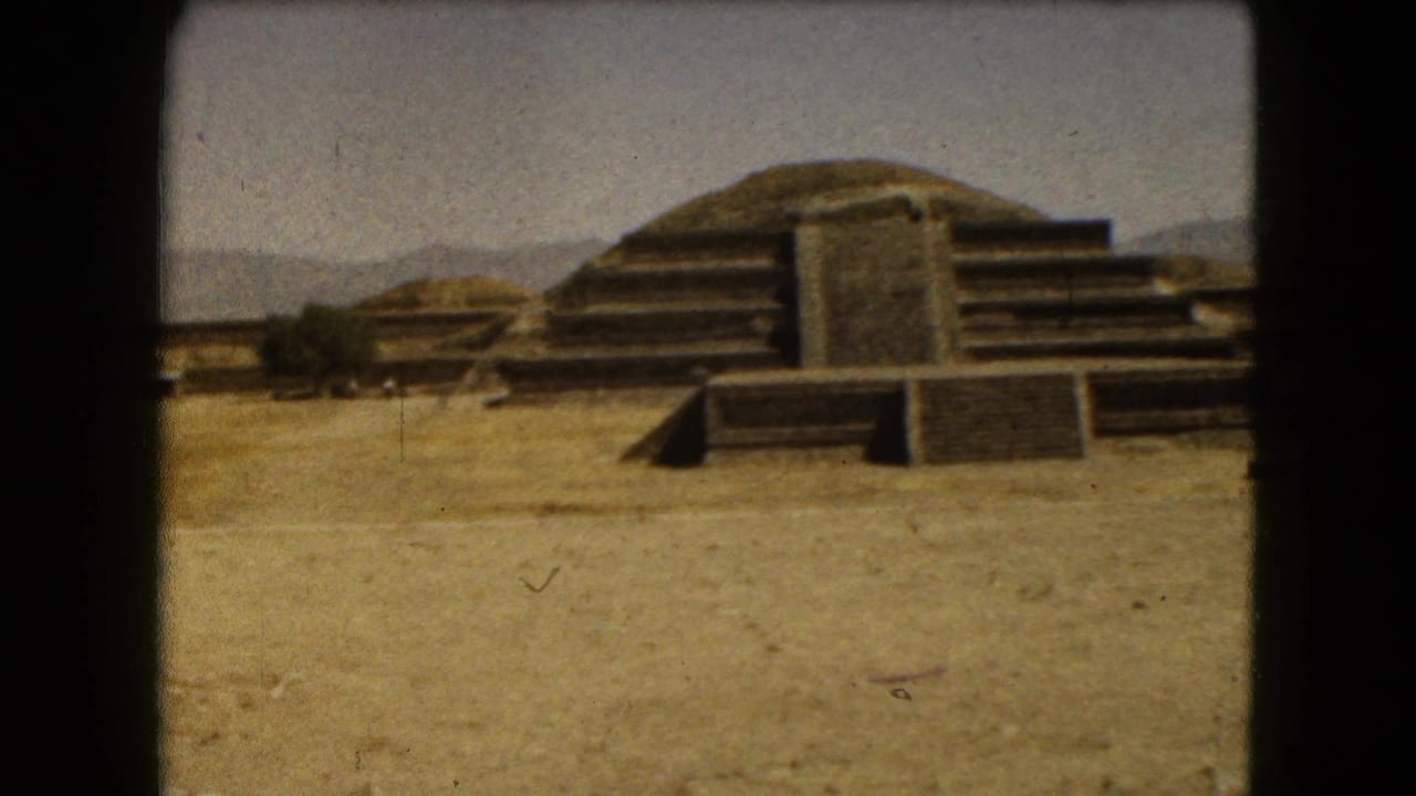 Wide 1962 Mexico City home-movie view of stepped ruins, low stone platforms, dry ground, and distant hills.