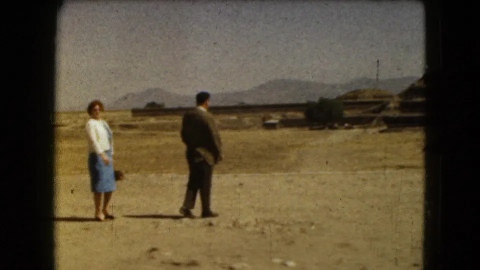1962 8mm frame near Mexico City showing the couple turned toward the ruin landscape, with mountains and low structures beyond.