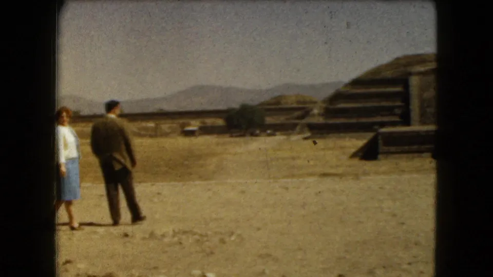 1962 8mm frame near Mexico City with the couple at left and larger stepped archaeological structures visible at right.