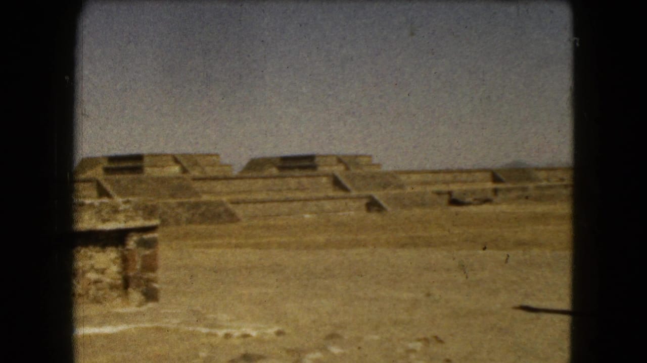 Wide view of sandy archaeological grounds with stepped stone structures under a pale sky.