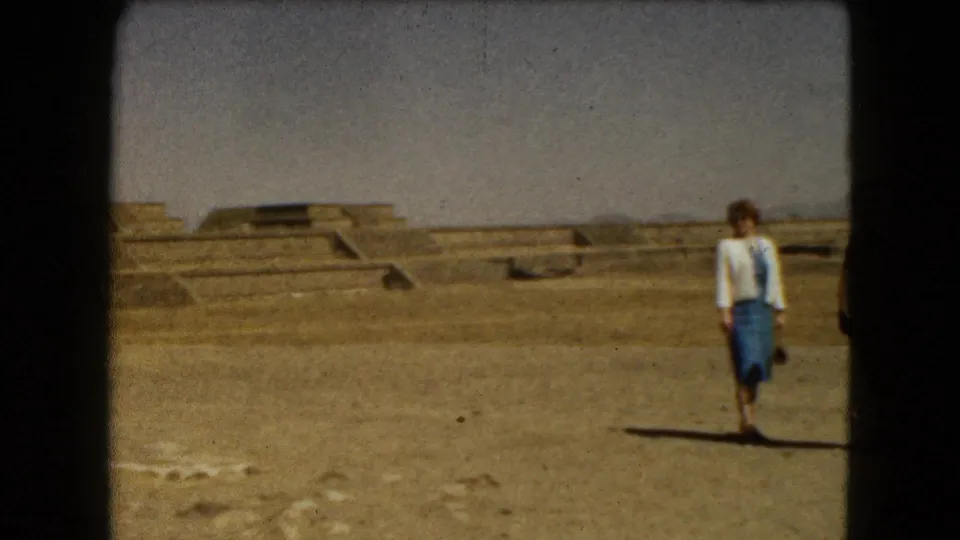 A woman walks through the Mexico City archaeological site, with stepped stone platforms visible behind her.