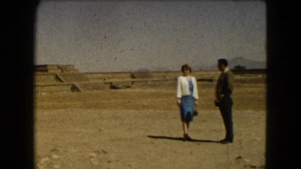 A man and woman stand together at the Mexico City archaeological site, framed by low stone platforms and open sky.