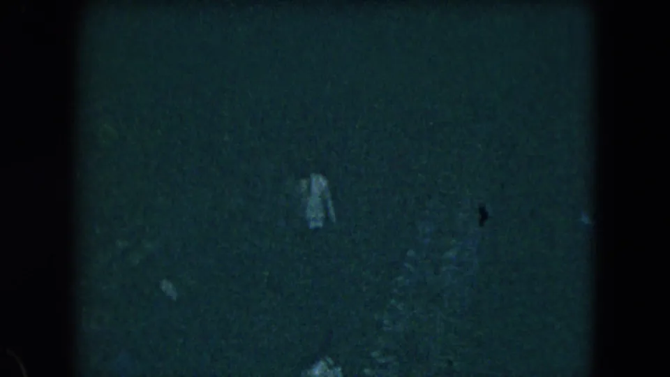 A faint person appears in deep shadow within grainy 1962 Mexico City 8mm footage, with details largely obscured.