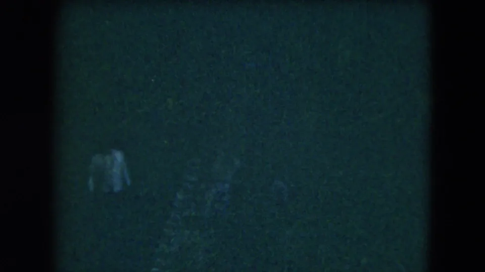 A distant, indistinct figure stands or walks in a dark 1962 Mexico City home-movie frame with heavy grain.