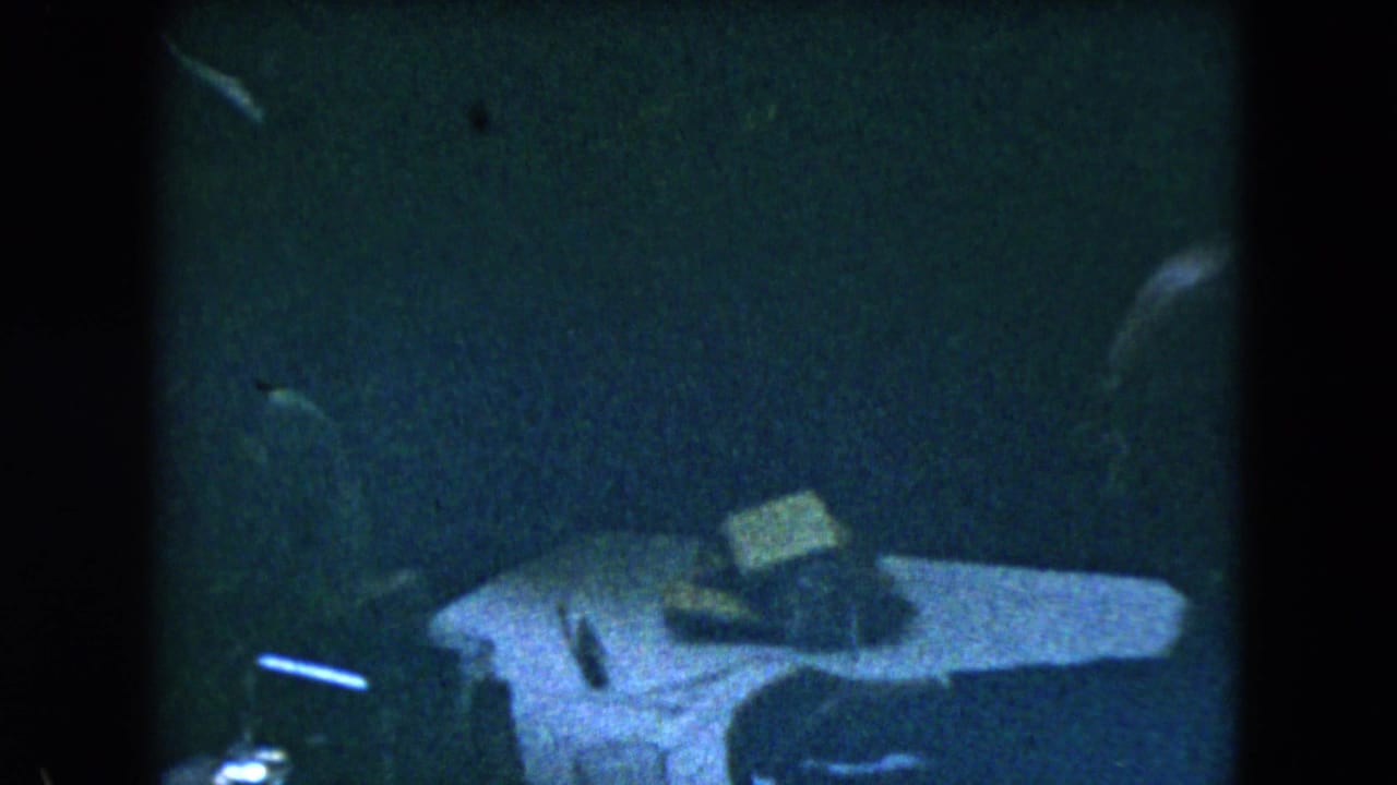 1962 Mexico City 8mm frame showing a dim table area with indistinct objects and heavy shadow across the interior.