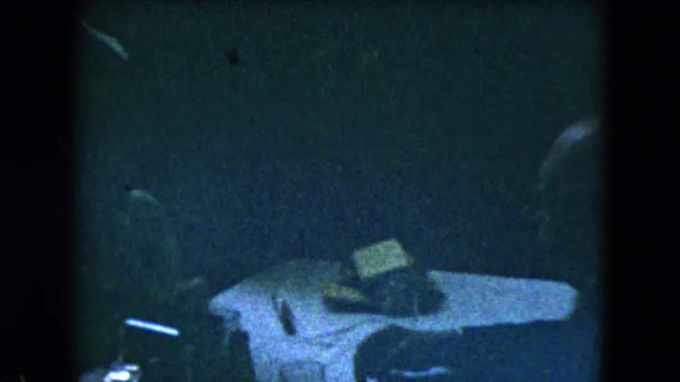 1962 Mexico City 8mm frame showing a dim table area with indistinct objects and heavy shadow across the interior.