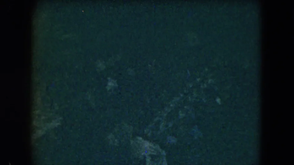 Dark 1962 Mexico City home-movie frame with vague human forms and dense 8mm grain obscuring room details.
